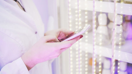 Close up of woman s hand with red finger nails texting or making notes in a lab standing next to a closet with test tubes.の写真素材