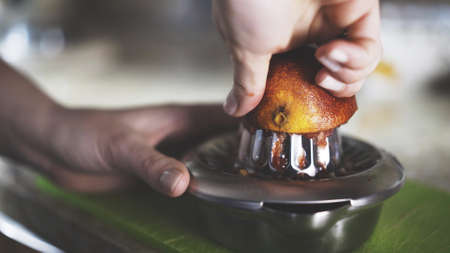 A hand squeezing juice from an orange on a manual glass squeezer. Side view. Kitchen background.の写真素材