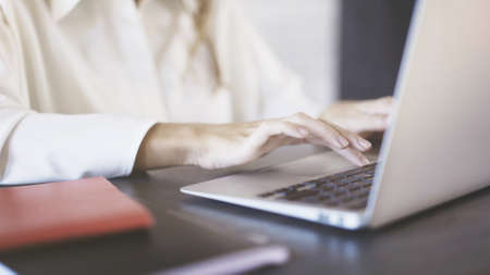 Close up of a woman wearing a white shirt typing and using a laptop touchpad in an office. Businesspeople concept.の写真素材