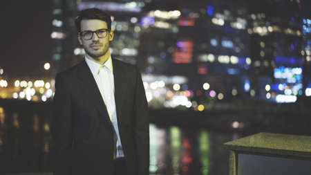 A young businessman dressed in a black suit at street at night time, downtown and on the backgroundの写真素材