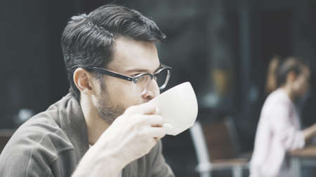 A closeup profile of a handsome man in eyeglasses drinking a cup of coffee at cafe outdoorsの写真素材