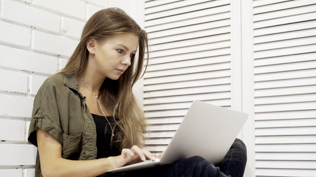 A closeup of young concentrated girl with long hair student dressed in a green shirt and jeans is...