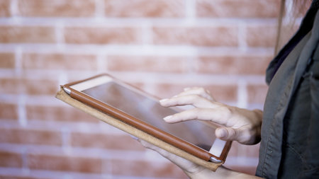 A young girl using modern digital tablet on the background of brick wall in the corrider, hipster girl typing on touch screen of tablet pcの写真素材