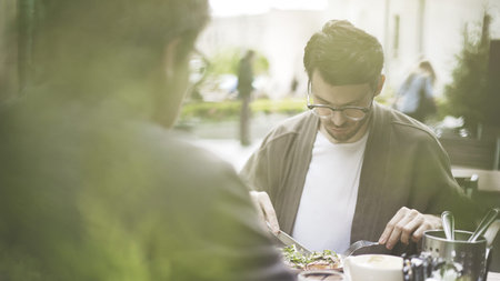 A handsome bearded man in eyeglasses eating fresh salad at cafe outdoors