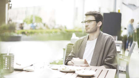 A handsome bearded man wearing eyeglasses sitting at cafe drinking coffeeの写真素材