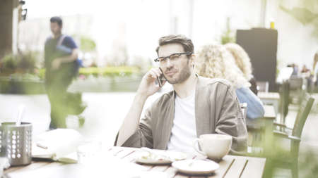 A handsome smiling man is talking on the phone at cafe outdoorsの写真素材