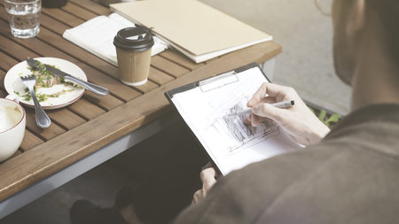 A closeup of man is drawing a sketch making notes at cafe outdoors drinking coffee during lunch time