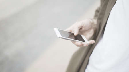 A closeup of white phone, a man holding a white smartphone on the street outdoorsの写真素材