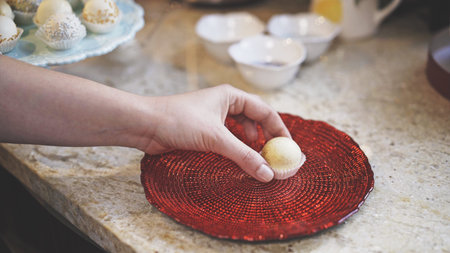 A woman hands, takes a white chocolate sweet covered with glitter. A sweet is lying on a beautiful red glass plateの写真素材