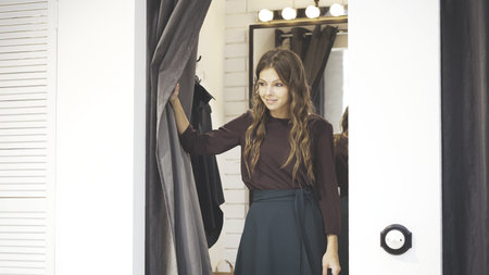 Young wavy hair woman trying on a blouse and a skirt in a shop dressing room. Concept of shopping