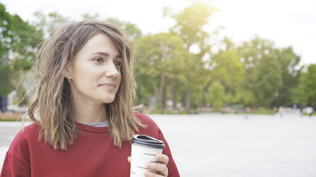 A closeup of young pretty cute casual brunette girl in a red sweatshirt is holding a cup of coffee...