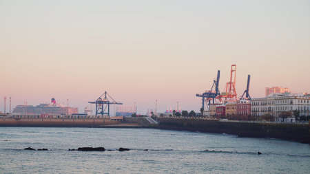 Gimbal shot of Cadiz pier and a cruise ship leaving from bay during evening pink orange sunset. Cadiz bay with a giant cruise ship sailingの写真素材
