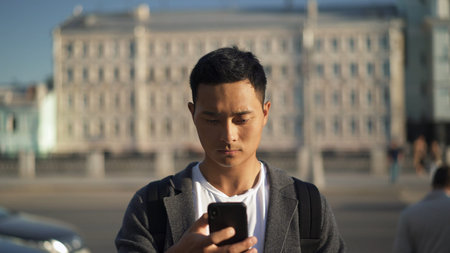 Pensive young Asian man looking at phone in Moscow. Tourist in Moscow. Freelance concept.の写真素材