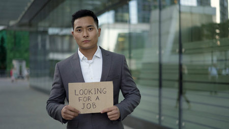 A young handsome Asian man in a suit standing on the street with a sign - Looking for a job....