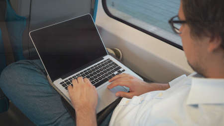 Young businessman with dark hair using his laptop while riding a train to workの写真素材