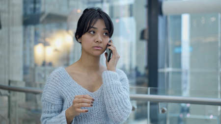 Portrait close up handheld shot of smiling happy black hair asian female standing and holding scrolling a phone on background of hitech officeの写真素材