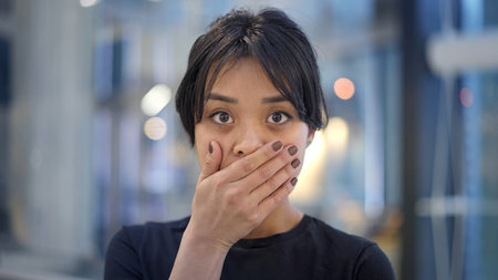 Portrait of attractive scared asian female with her hand nearby her mouth. problem concept or...