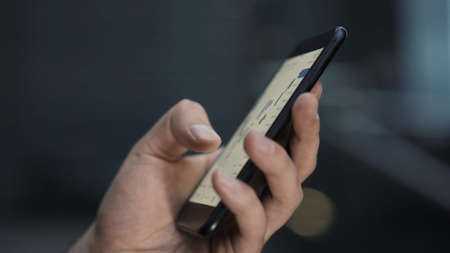 Checking stock market on the phone on background of blurred business buildings. Close up of a left hand with a phone, stock market graphs, the device on blurry blue backgroundの写真素材