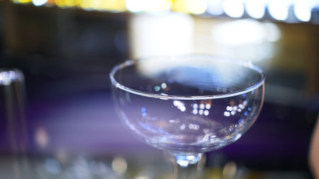 Empty cocktail glass on a bar counter, close up lens flare. Cocktail glass focused shot inside on...