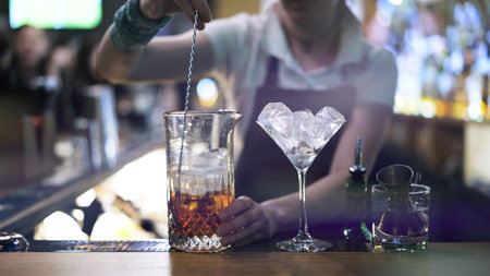 Cocktail glass with cubes of ice , close up, on blurry background of barman at bar. Cocktail glass...