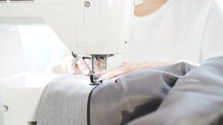 Female hands sew on a white sewing machine close-up. Concept of sewing courses, woman in white...