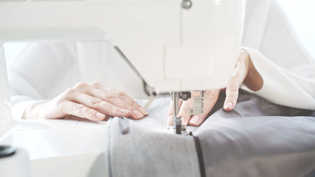 Female hands on a white sewing machine close-up. Concept of sewing in modern bright studio, woman in...