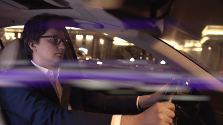 Man driver in black suit and eyeglasses holding the wheel. Middle shot of driver at night,...