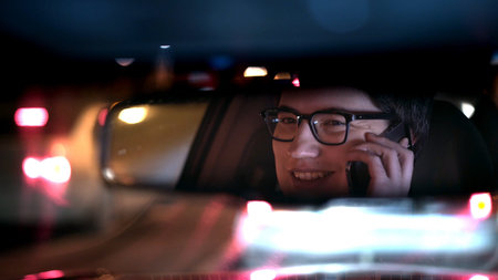 Driver talking on the phone, reflected in a rear view mirror, night shot. Driver in a mirror in car,...