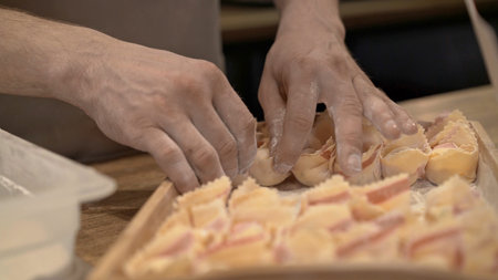 Male hands laying tortellini on wooden tray, on wooden kitchen table close up. Male hands cooking...
