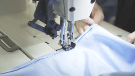 Sewing on machine, hands and blue cloth close up. Lens flare of sewing process, female hands on white machine with blurry effect side shotの写真素材