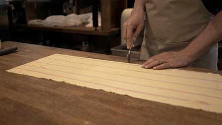 Male hands cutting dough rolled on big wooden table at the restaurant kitchen. Making ravioli,...