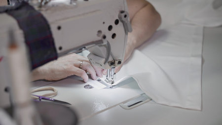 Female hands sew on a white sewing machine close-up. Concept of sewing in modern bright studio,...