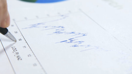 Man writing on a paper with graph closeup. Holding black pen on a blue graph of a research, macro...