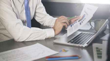 Businessman male hands in white shirt and tie look through graphs and papers in the office. Man no face making project holding reading papers, graphs, pens and pencilの写真素材