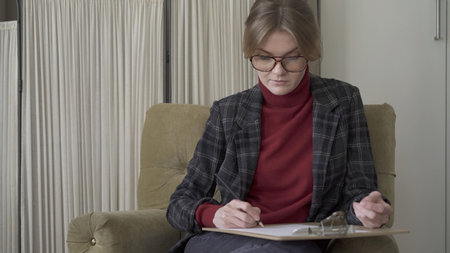 Female manager in eyeglasses sitting in chair, middle shot, making notes looking at the papers on...