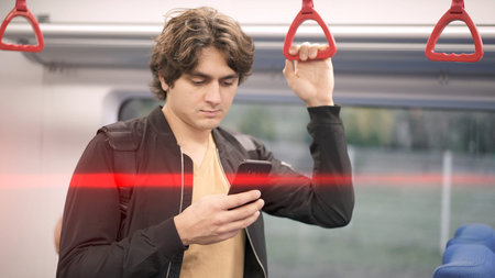 Man holding by red handrails in train, man typing in phone on background of white train car. Middle...