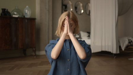 Woman doing breathing exercises, yoga practicing. Blonde attractive physical trainer at home interior with bed on backgroundの写真素材