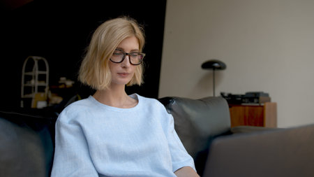 Pensive woman sitting on sofa and working with laptop, living room, work from home concept