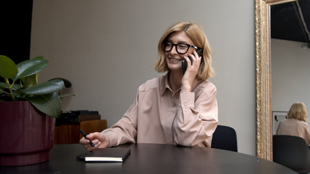 Adult woman in eyeglasses, laughing wearing pink shirt calling on the smartphone. Concept of conversation.の写真素材