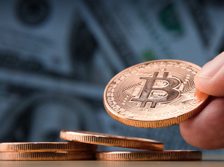 Female hand showing bitcoin coin.Dollar banknotes as a background.Virtual cryptocurrency...