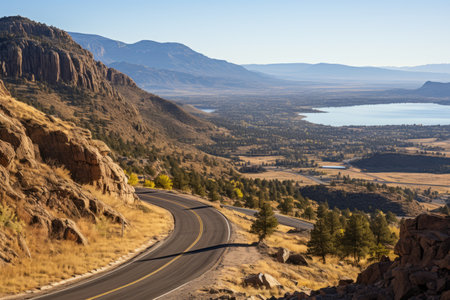 A road winding through the hills. The sky in the distance and a lake in the valley below. Blue hazy sky in the background. Coniferous trees on hillsidesの素材