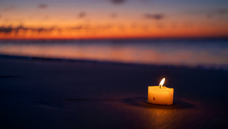 A lit candle rests on the sandy beach, casting a warm glow against the backdrop of a stunning sunset, with vibrant colors reflecting on the water, creating a serene atmosphereの素材