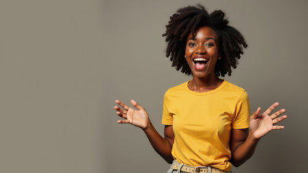 African american woman wearing a bright yellow shirt is smiling widely with hands raised in excitement, showcasing a lively and cheerful atmosphere, perfect for expressing happiness and positivityの素材