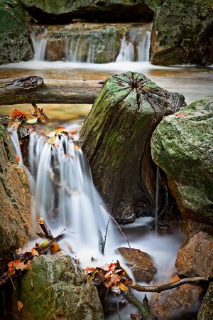 rocks and wood in autumn river rapid long exposure results in smooth surface and surreal blurred waterの写真素材