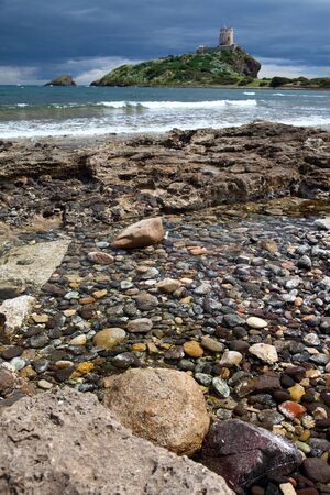 Roman tower on Island Sardinia Italy sea dramatic sky and clouds rocks in surfの写真素材