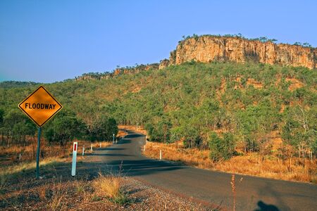 floodway warning road sign at Australian outback Northern territory the bush with dry vegetation just before the rainy season with gentle hills and rocky slopesの写真素材