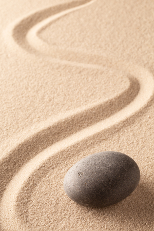 curved line in the sand of a zen stone garden. A round black rock on sandy background. Concept for spirituality, harmony and balance.の写真素材