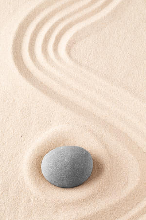 Zen garden meditation stone. Round rock on sandy texture background. Yoga or mindfulness concept.