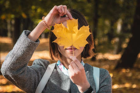 Autumn yellow leaf in the girls hand in front of her face.の写真素材