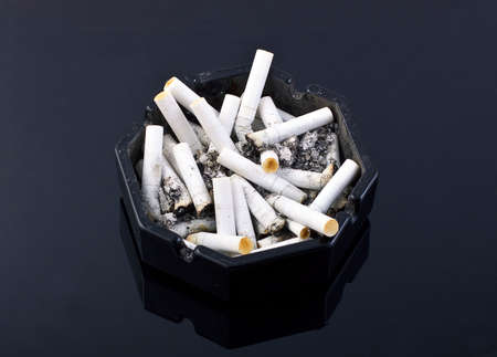 black ashtray with cigaretes on black tableの写真素材